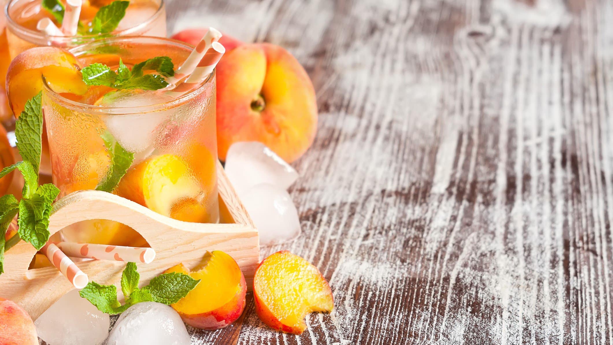 Pfirsich-Bowle mit Eis und Früchten in Gläsern auf Holzuntergrund.