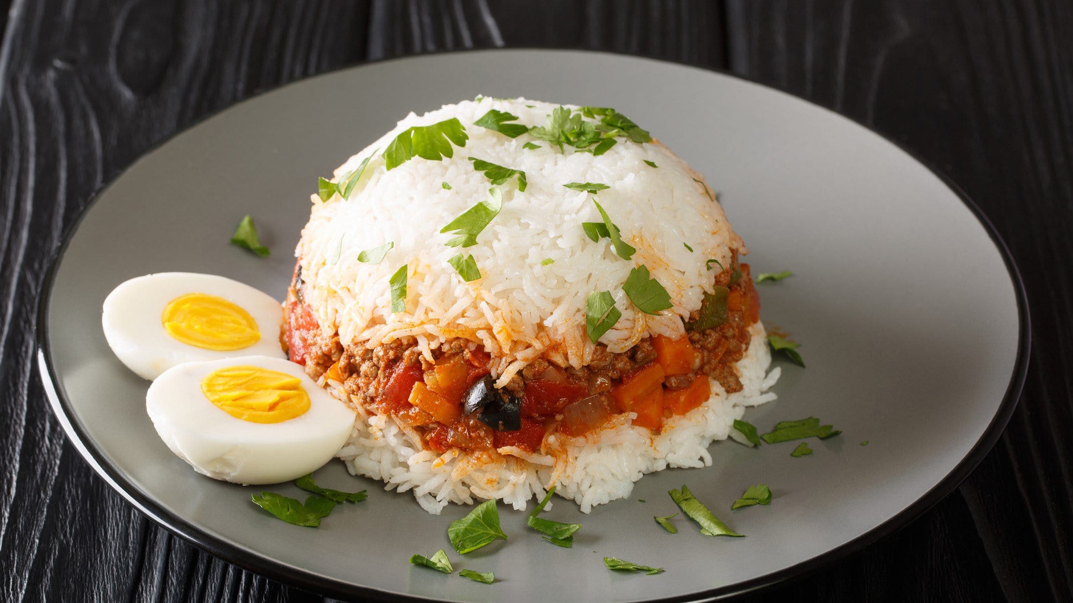 Arroz Tapado peruanischer Reis mit Hackfleisch und Ei auf grauem Teller auf schwarzem Untergrund. Draufsicht.