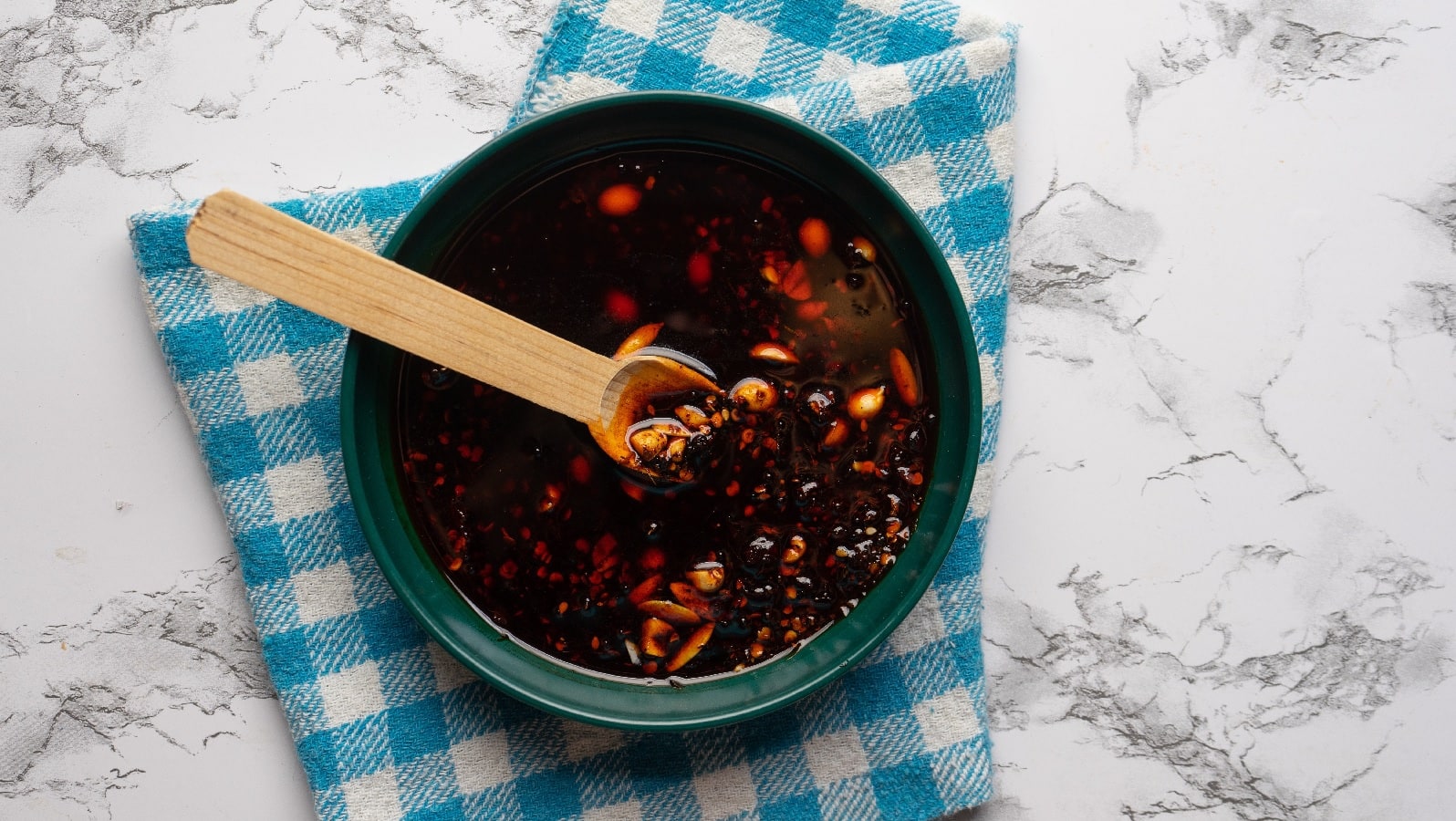 Ein Glas selbst gemachtes Sichuan-Chiliöl auf einem blau karierten Küchentuch