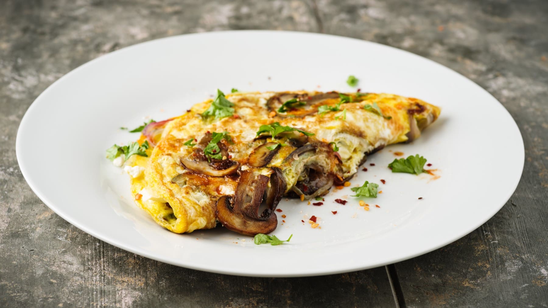 Omelett mit Champignons und Feta auf einem weißen Teller auf einem hölzernen Untergrund.