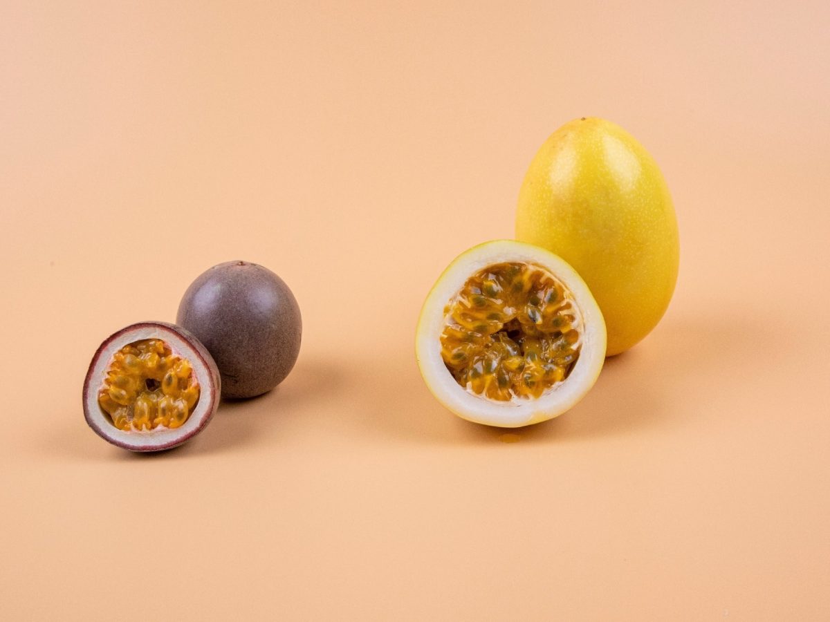 Eine angeschnittene Passionsfrucht und eine angeschnittene Maracuja vor einem apricot-farbigen Hintergrund.