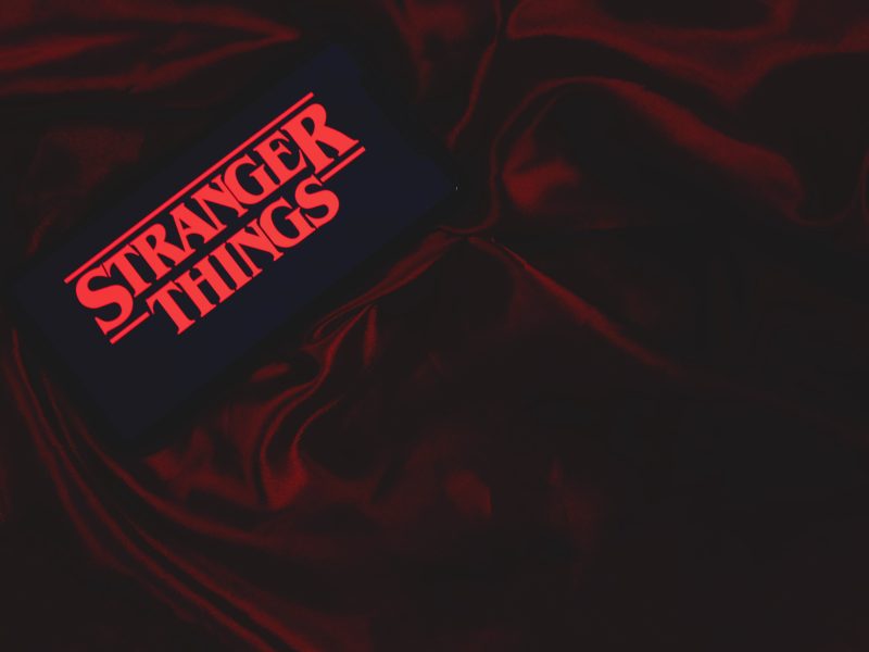 80er Jahre Retro-Menü zur vierten Staffel Stranger Things roter Schriftzug auf Mobiltelefon auf roter Samtdecke. Aufnahme aus der Vogelperspektive.