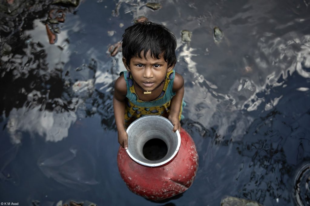 Ein kleines Mädchen sammelt Wasser in einem Slum in Bangladesh