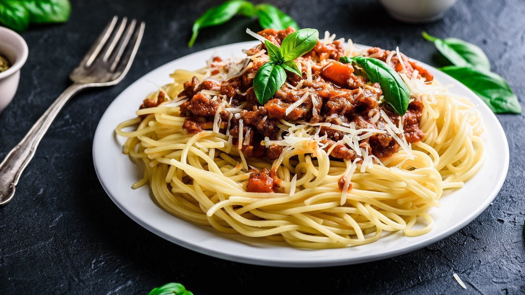 Spaghetti Bolognese bestreut mit Parmesan und Basilikum auf dunklem Untergrund