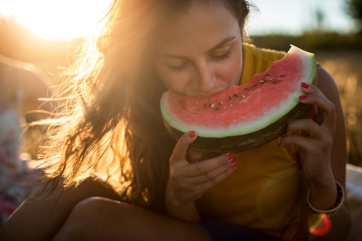 Eine junge Frau beißt beleuchtet von der Abendsonne in eine Scheibe Wassermelone.