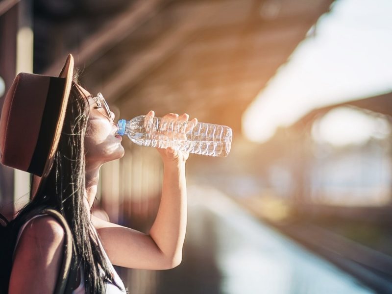Frau trinkt Wasser aus Flasche an einem sonnigen Bahnhof