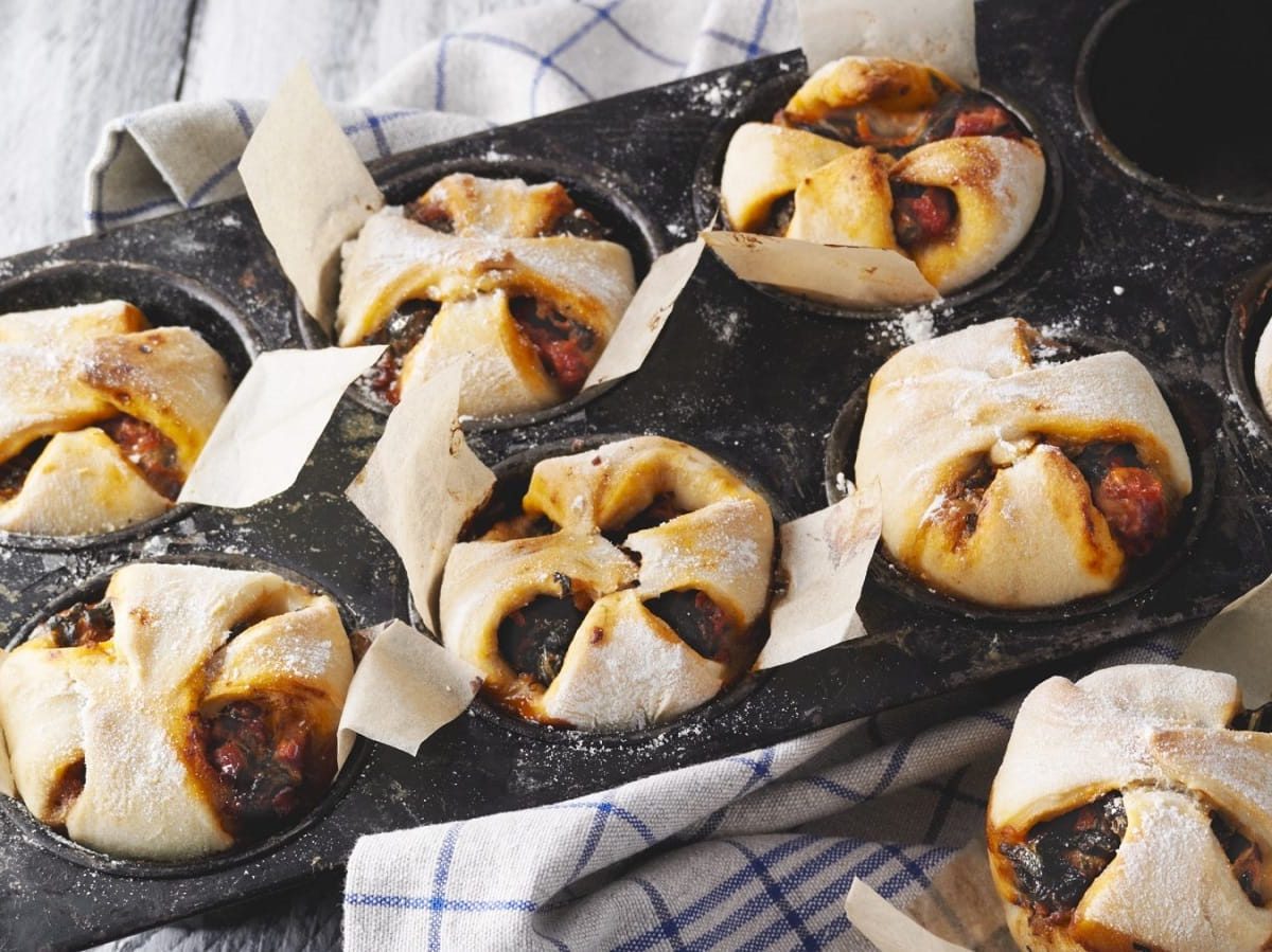 In Muffinformen sind Pizza-Muffins mit Blattspinat und Speck gebacken. Man erkennt die Spinat Füllung.