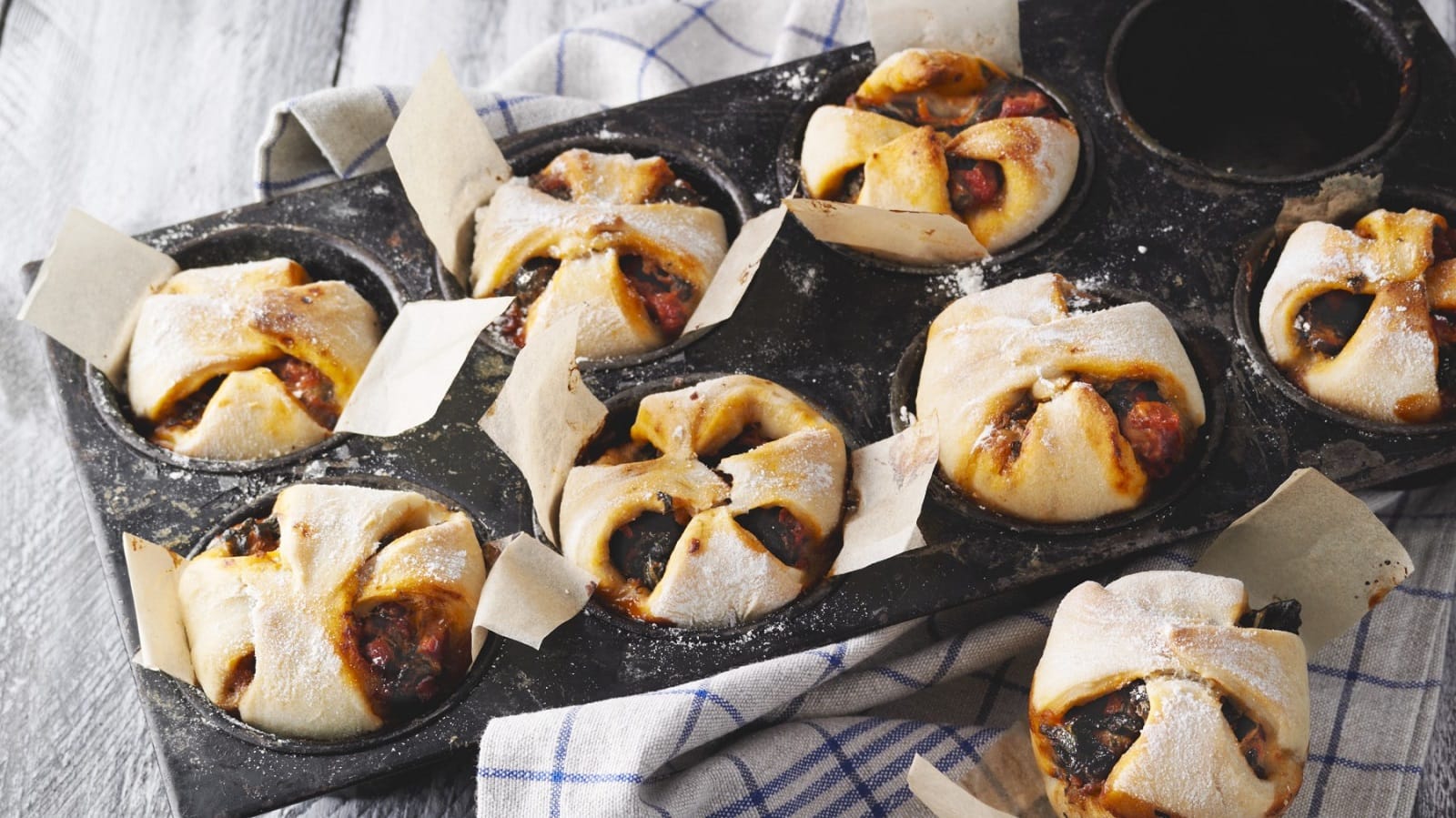 In Muffinformen sind Pizza-Muffins mit Blattspinat und Speck gebacken. Man erkennt die Spinat Füllung.