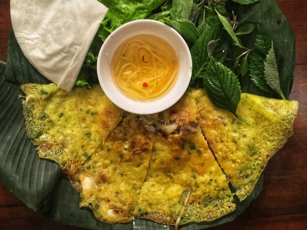 Vegane Banh xeo auf einem Teller neben frischen Kräutern und einer Sauce