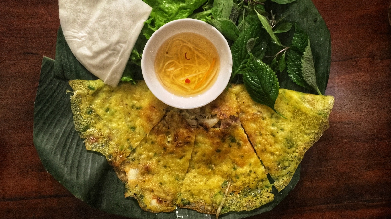 Vegane Banh xeo auf einem Teller neben frischen Kräutern und einer Sauce