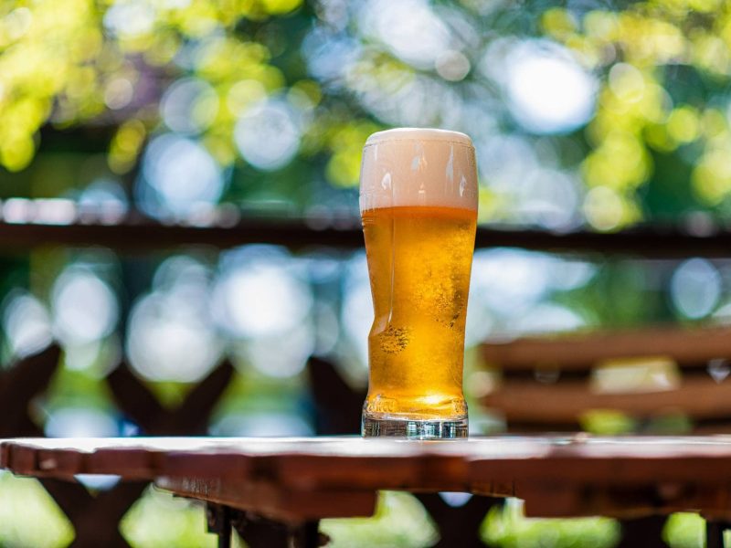 Biergärten Berlin: ein volles Bierglas auf einem Holztisch vor grünen Bäumen.