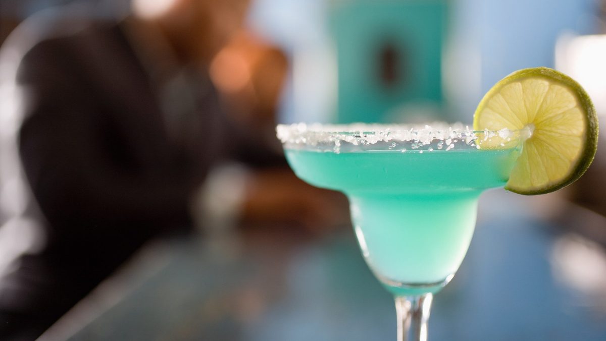 Gun Metal Blue Mezcal Cocktail auf Bar vor unscharfem Hintergrund. Frontalansicht.