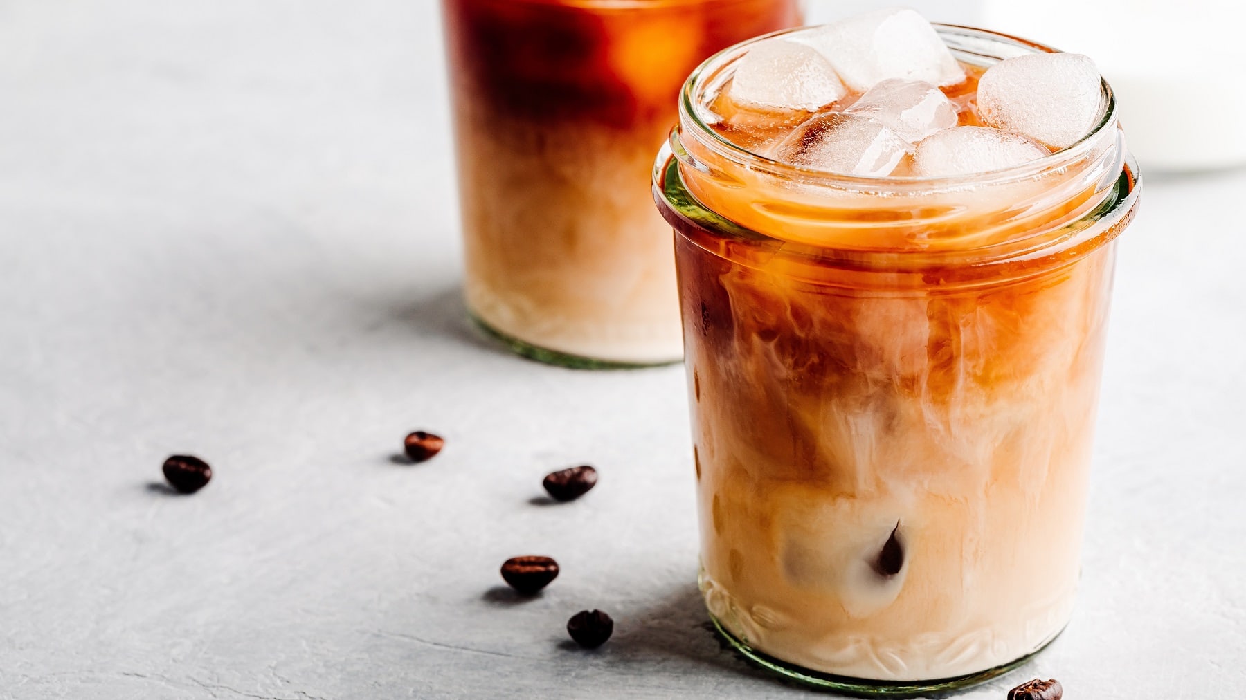 Ein Glas Iced Vanilla Latte mit Eiswürfeln, daneben liegen Kaffeebohnen.