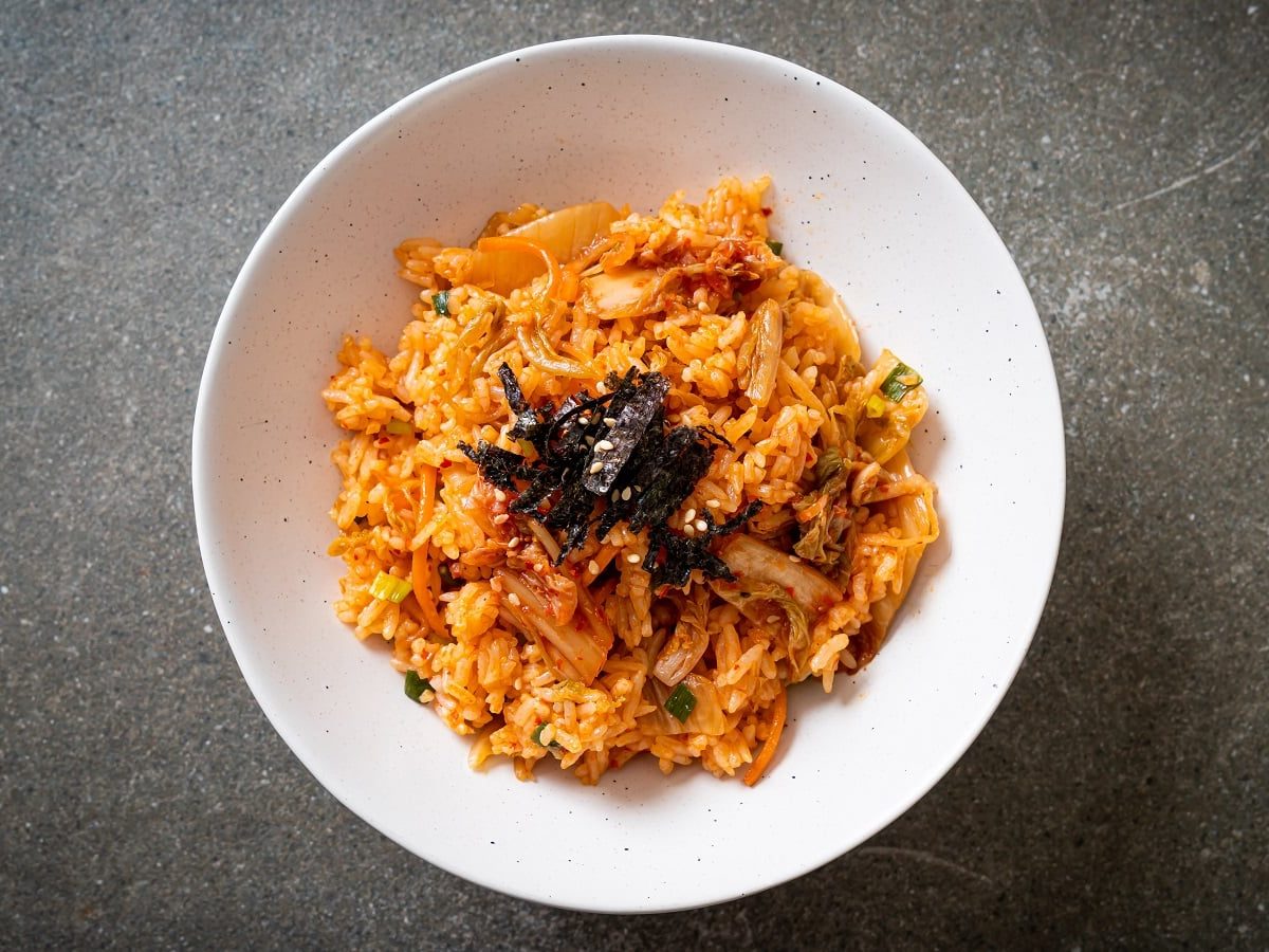 Ein Teller mit Kimchi Fried Rice und Nori-Streifen in einer weißen Schüssel auf grauem Hintergrund