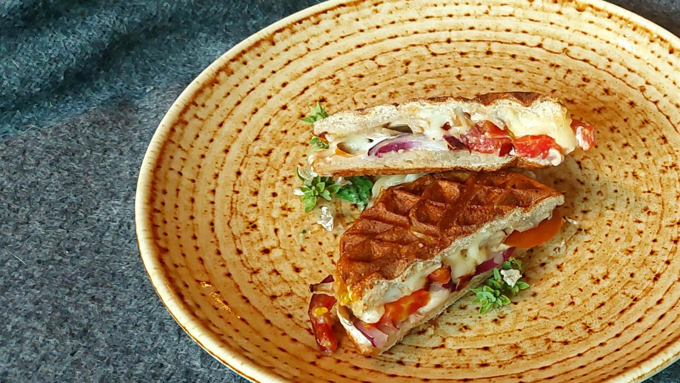 Ein hellbrauner Teller mit dem halbierten Laugen-Sandwich und grauem Untergrund.