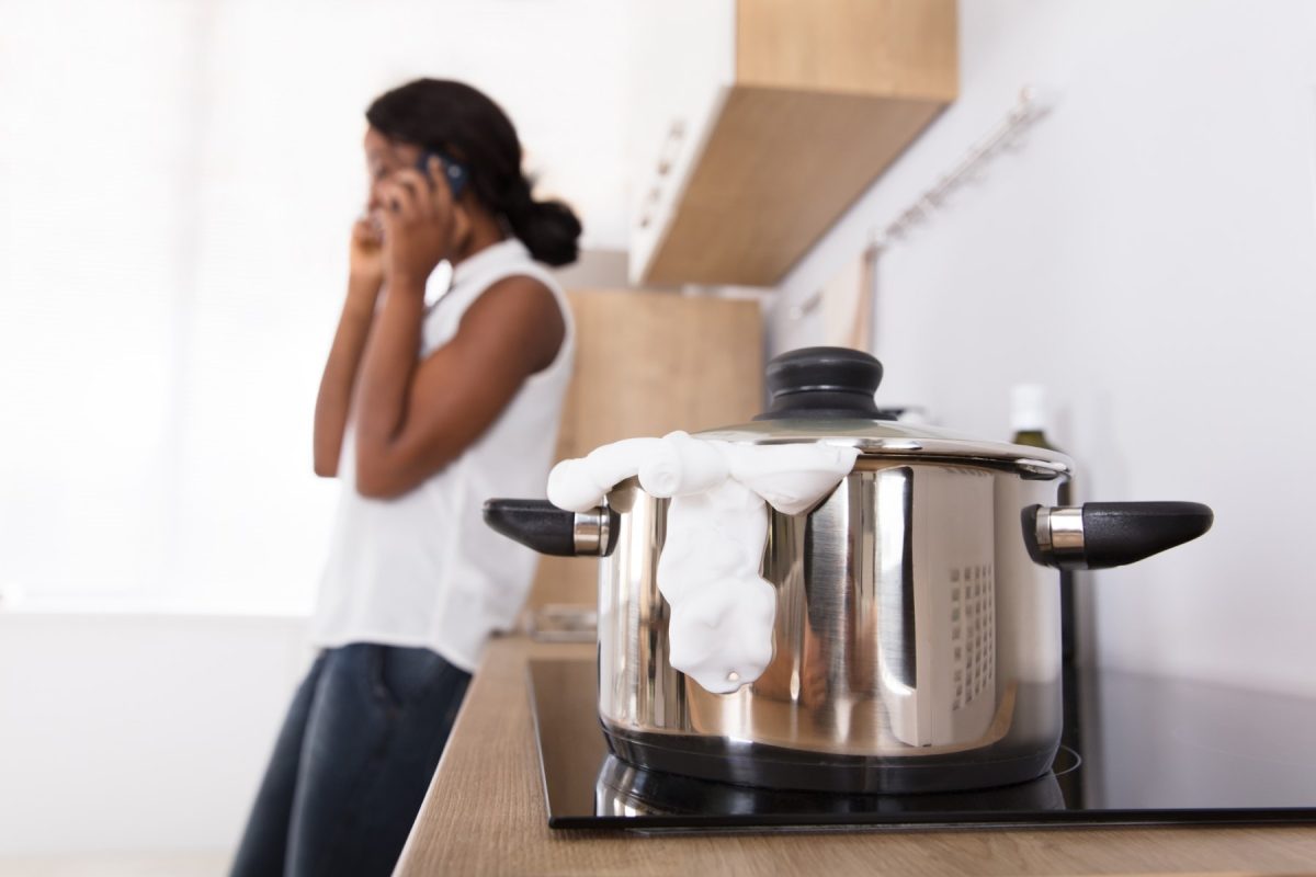Eine Frau telefoniert in der Küche während Milch in einem Topf überkocht.