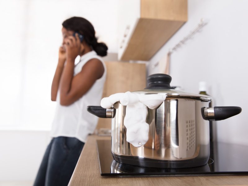 Eine Frau telefoniert in der Küche während Milch in einem Topf überkocht.
