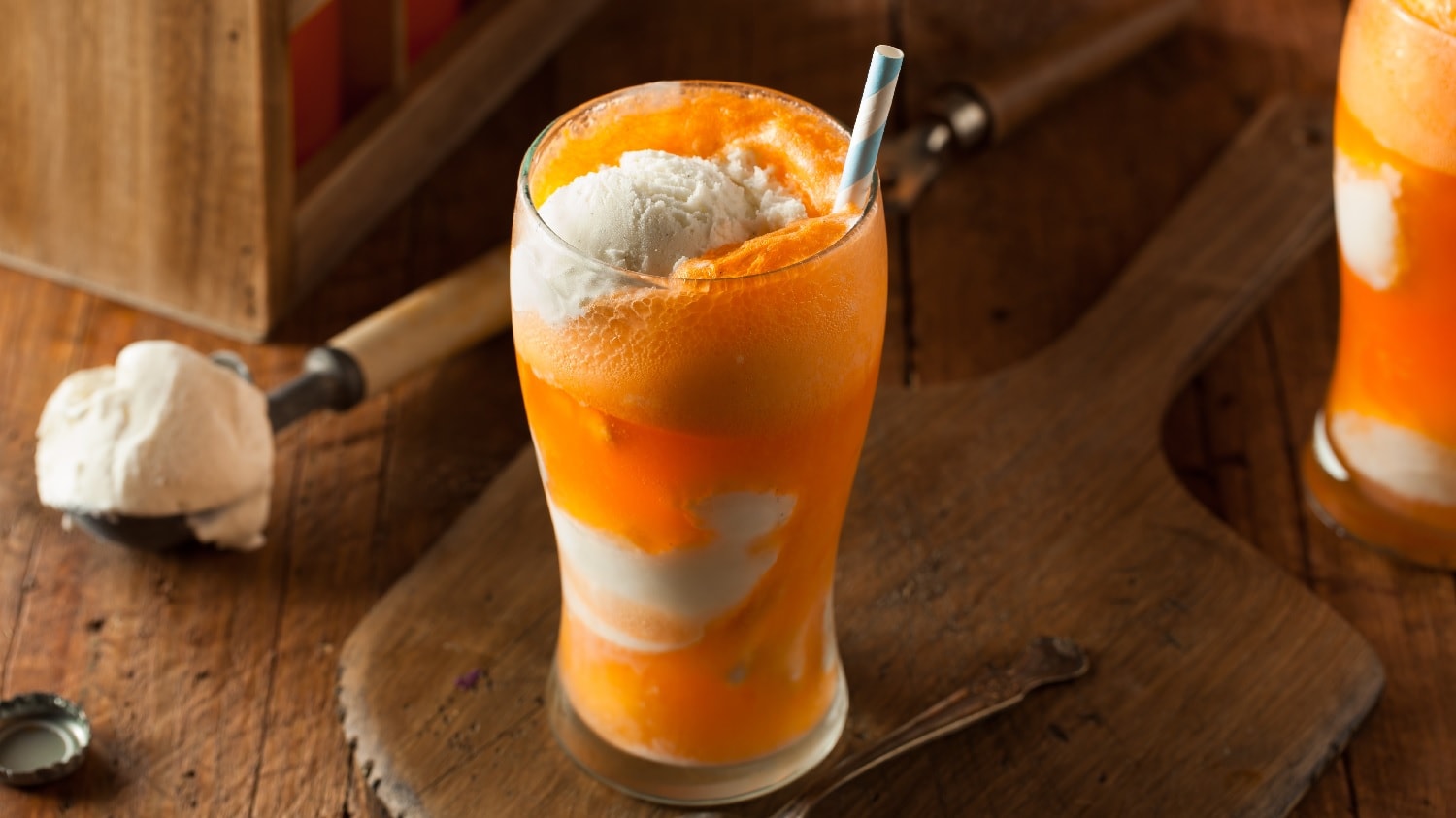 Ein großes Glas mit orange-weißer Schichtung der verschiedenen Orange Cream Float Zutaten. Alles auf einem dunklen Holztisch.