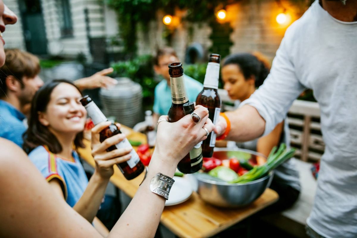 Pfingst-Grillen im Wildwuchs Brauwerk: eine Gruppe junger Menschen sitzt draußen an einem Tisch und stößt mit Bier an.