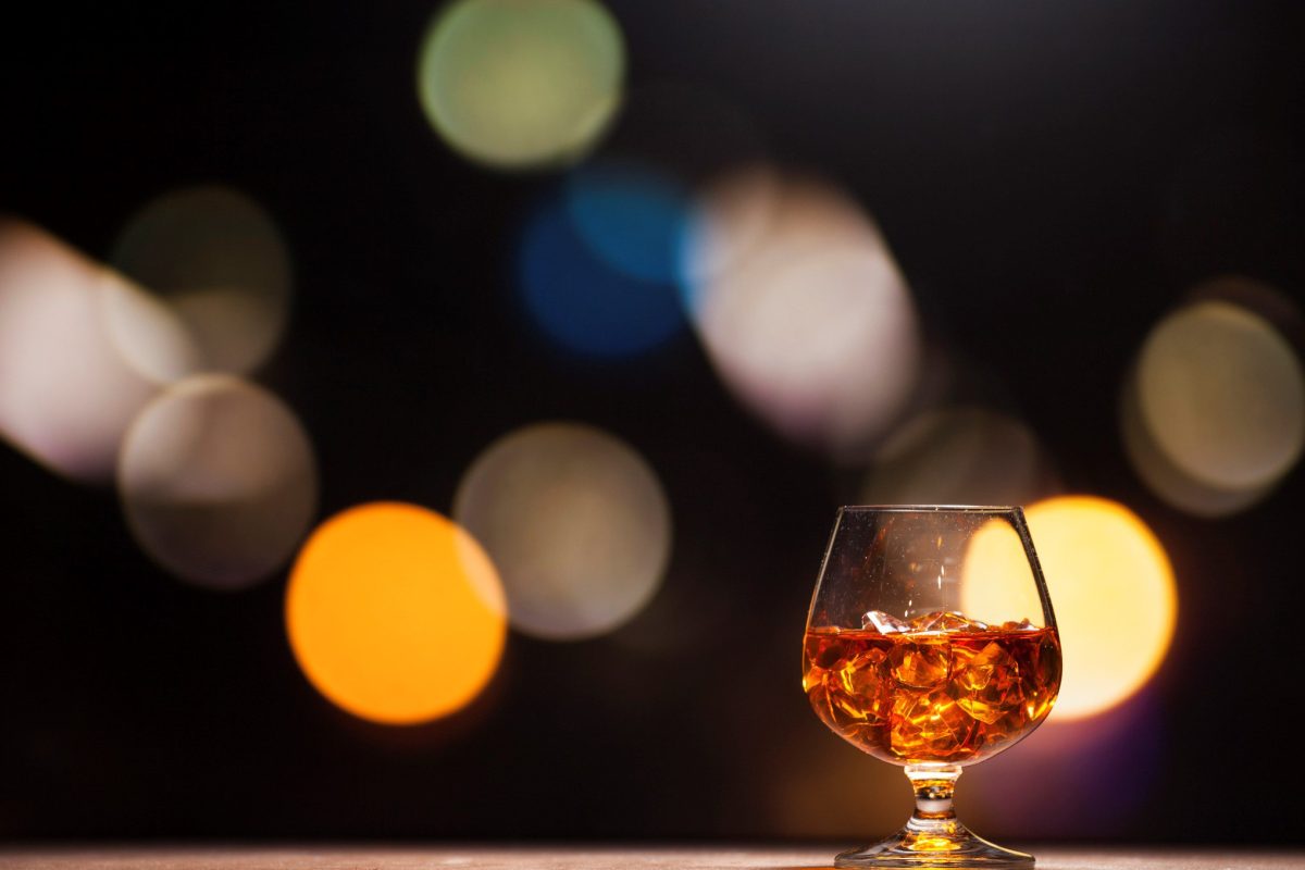 Zum Tag des deutschen Whiskys ein Glas deutscher Whisky in Berlin mit Eis vor unscharfem Stadtpanorama.
