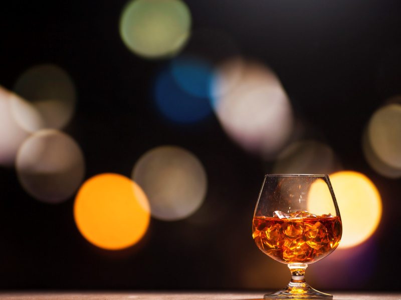 Zum Tag des deutschen Whiskys ein Glas deutscher Whisky in Berlin mit Eis vor unscharfem Stadtpanorama.