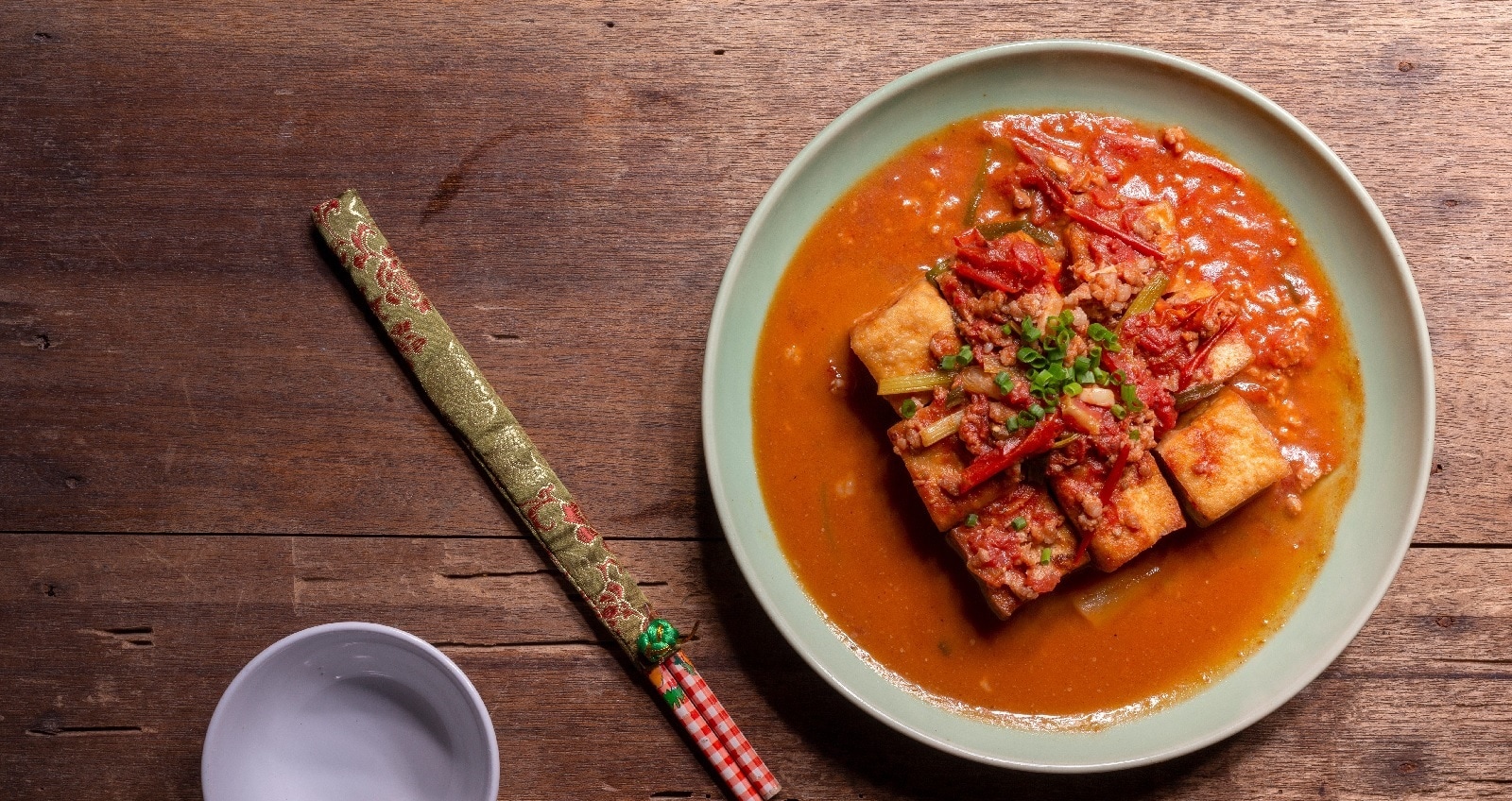 Eine Schüssel Tofu in Tomatensauce neben einem Paar Stäbcgen