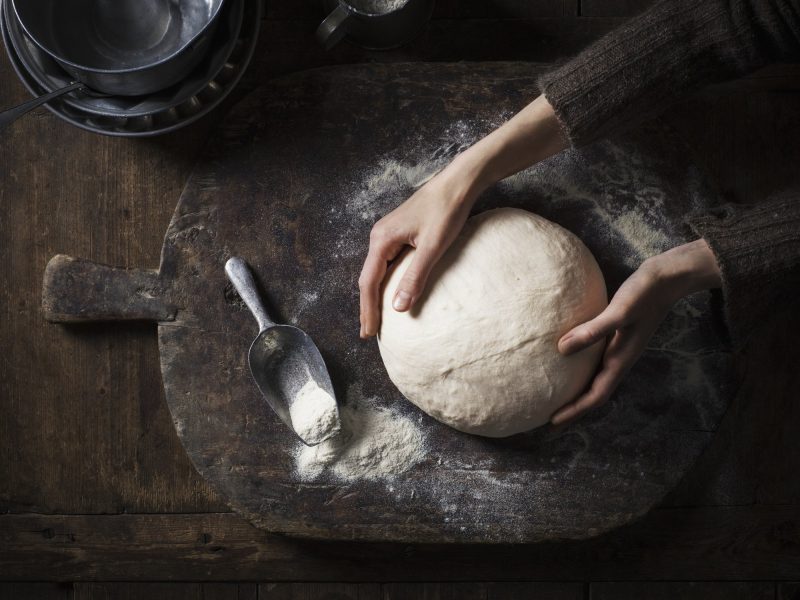 Tipps Brot backen: Frau formt einen Laib Brot auf dunklem Holzbrett