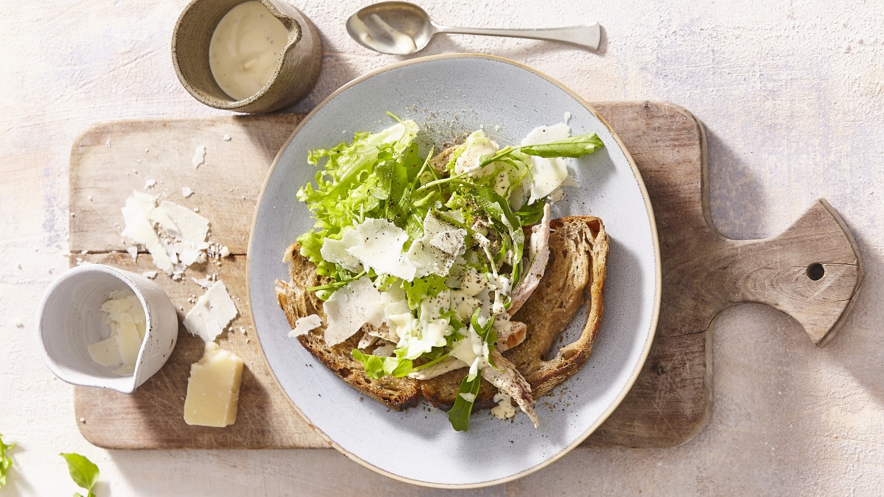 Grünes Caesar-Salat-Sandwich mit Parmesan, Geflügelbrust, Salat und selbstgemachtem Dressing auf rustikalen Bauernbrot, serviert auf einem weißen Teller auf einem Holzbrett.