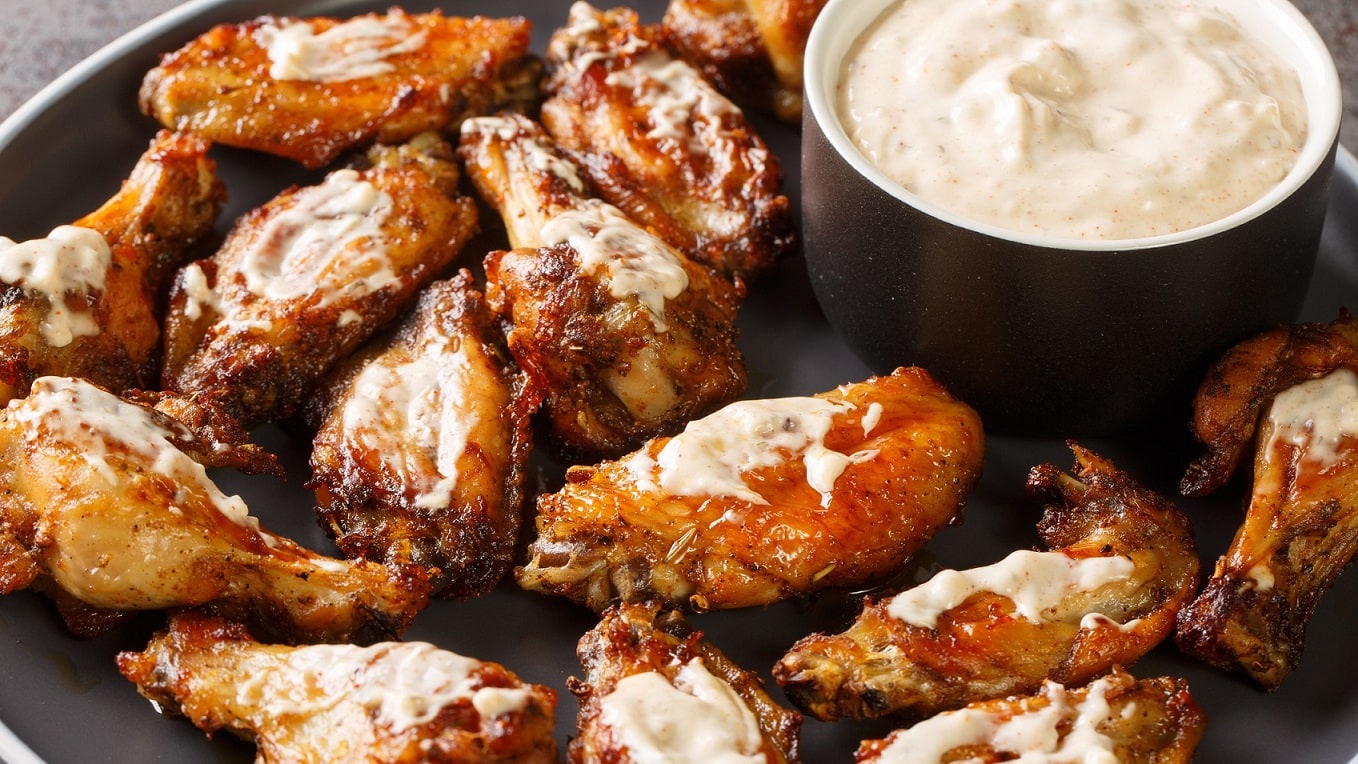 Chicken Wings vom Grill mit Rub und Alabama White Sauce auf schwarzem Teller aus der Draufsicht.