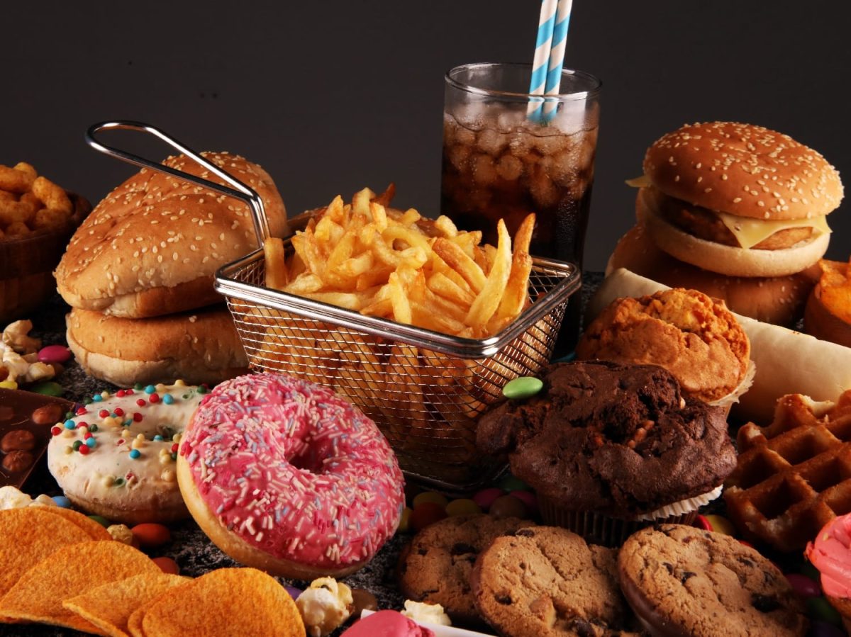 Viel Junkfood wie Burger, Cookis, Waffeln, Pommes und Donuts geballt auf und vor einem dunklem Unter- und Hintergrund.