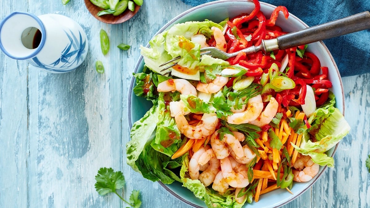 eine Schüssel Salat mit Shrimps und asiatischem Dressing steht auf einem hellblauen Untergrund aus Holz.