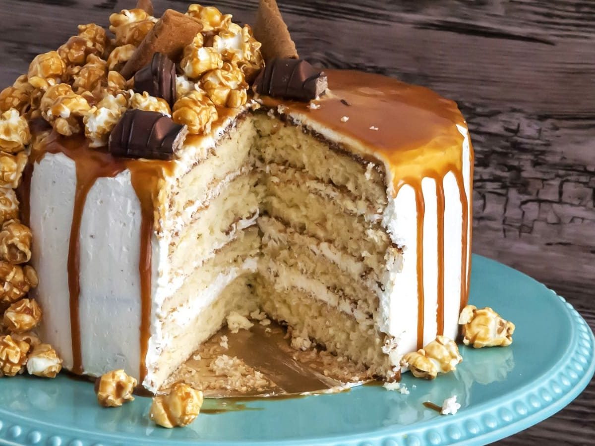 Auf einem Teller steht ein Drip Cake mit Karamell und Popcorn. Er ist mit Popcorn und Schokoriegeln dekoriert.