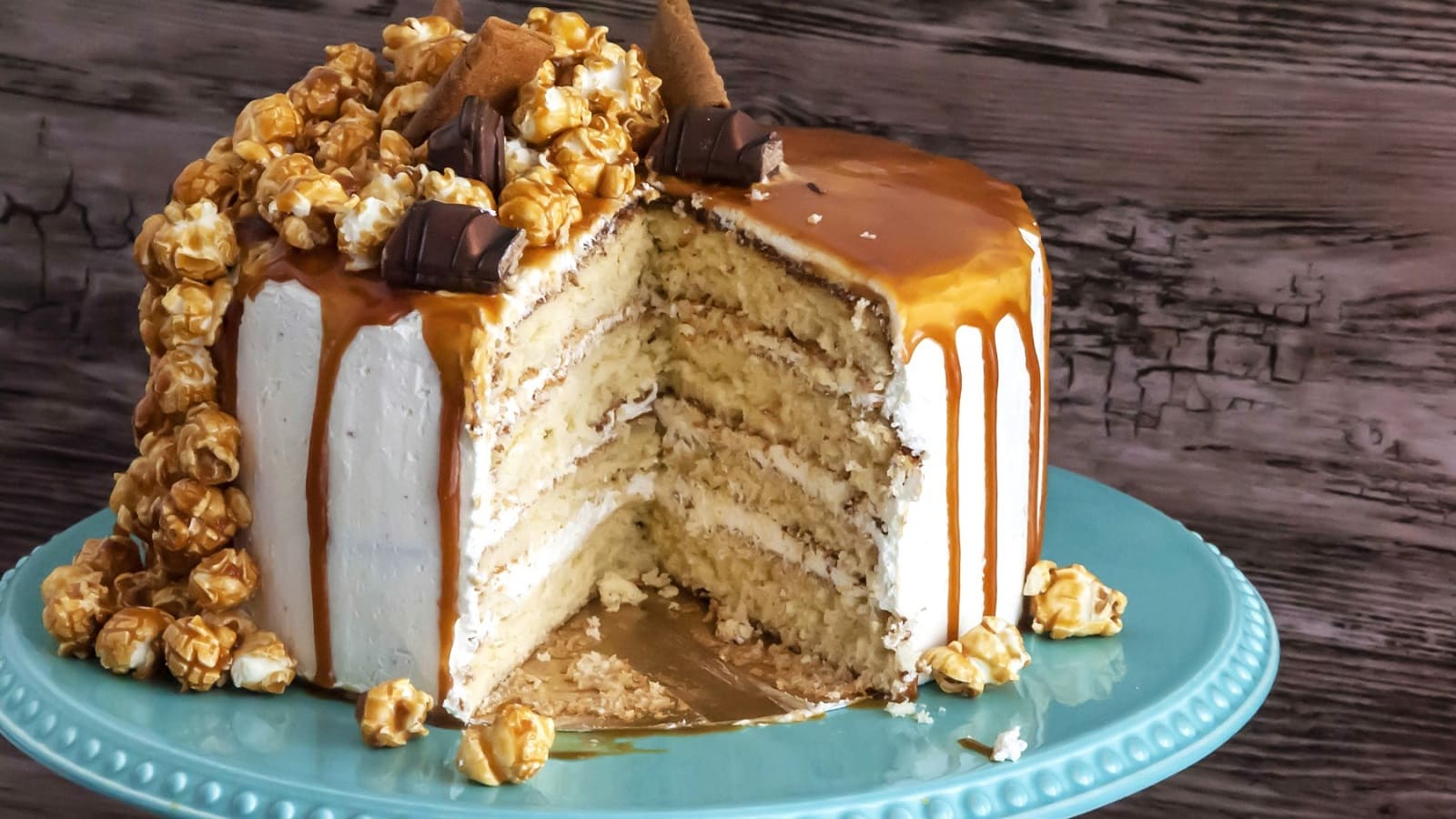 Auf einem Teller steht ein Drip Cake mit Karamell und Popcorn. Er ist mit Popcorn und Schokoriegeln dekoriert.