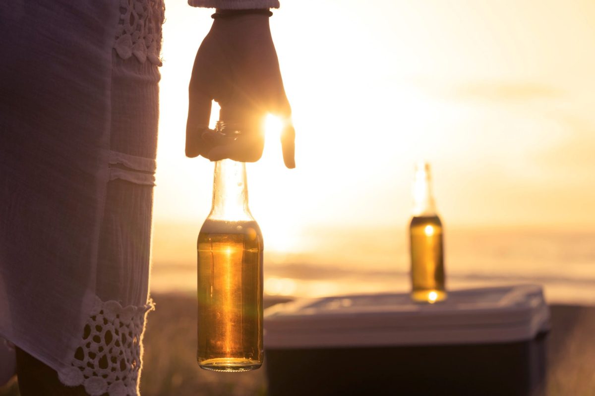 Frau hält Bier im Sonnenuntergang. Vor ihr steht eine weitere Flasche!