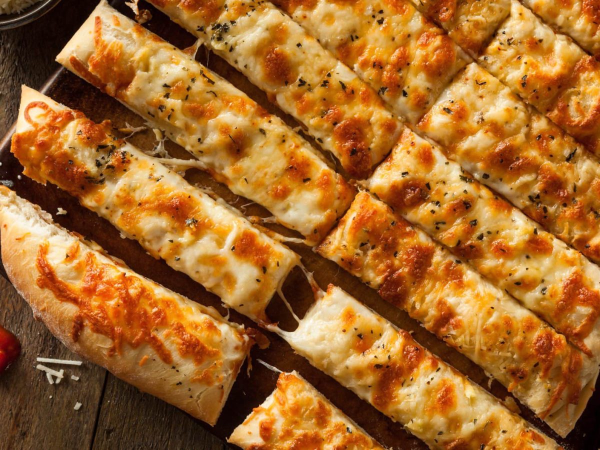 In Streifen geschnittene Pizzastangen mit Käse auf Holzuntergrund.