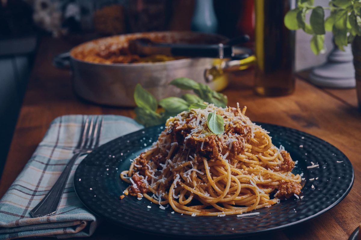 Spaghetti Bolognese bestreut mit Kräutern und Parmesan auf dunklem Teller
