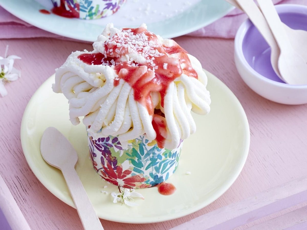 Auf einem kleinen Teller steht eine Portion der Spaghettieis-Cupcakes. Er ist mit Erdbeersauce und weißer Schokolade verziert.