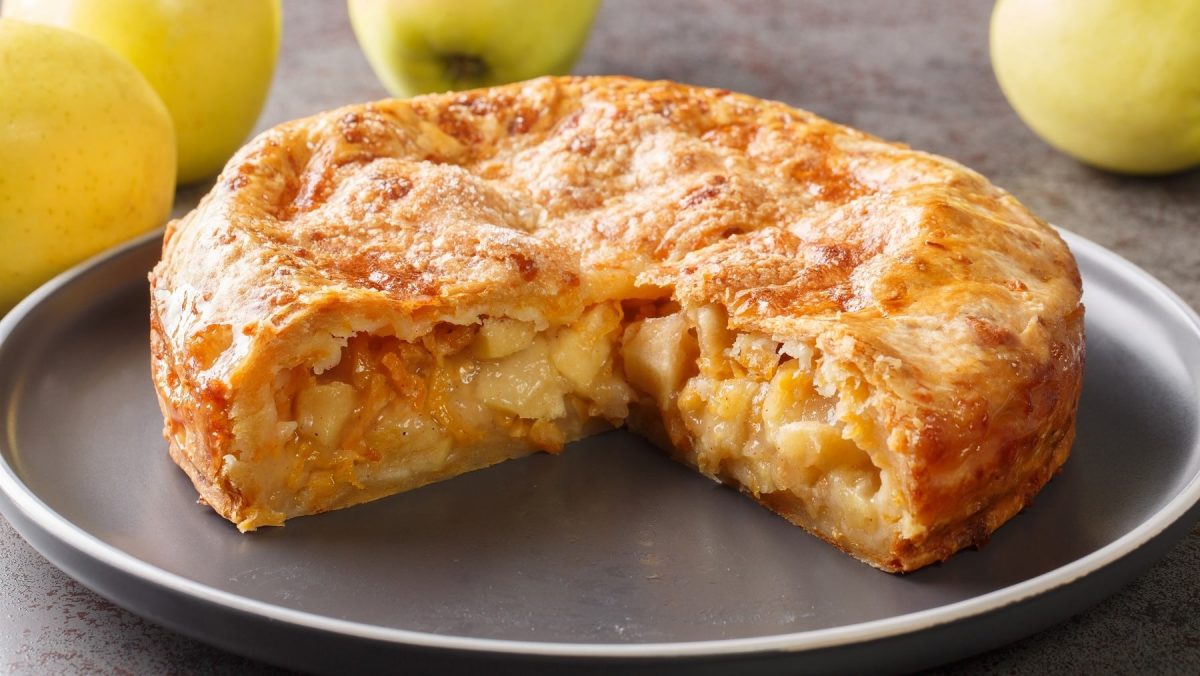 Angeschnittener Apple-Cheddar-Pie, gefüllt mit Apfelstücken und überbacken mit einer Käsekruste, serviert auf einem grauen großen Teller auf einem einfachen schwarzen Tisch.