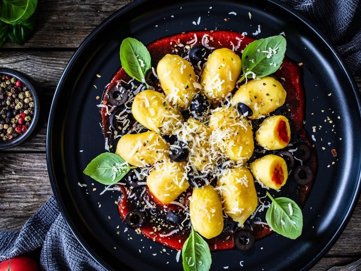 Ein Teller gefüllte Gnocchi mit rotem Pesto, Basilikumblättern, Parmesan und Oliven in der Draufsicht