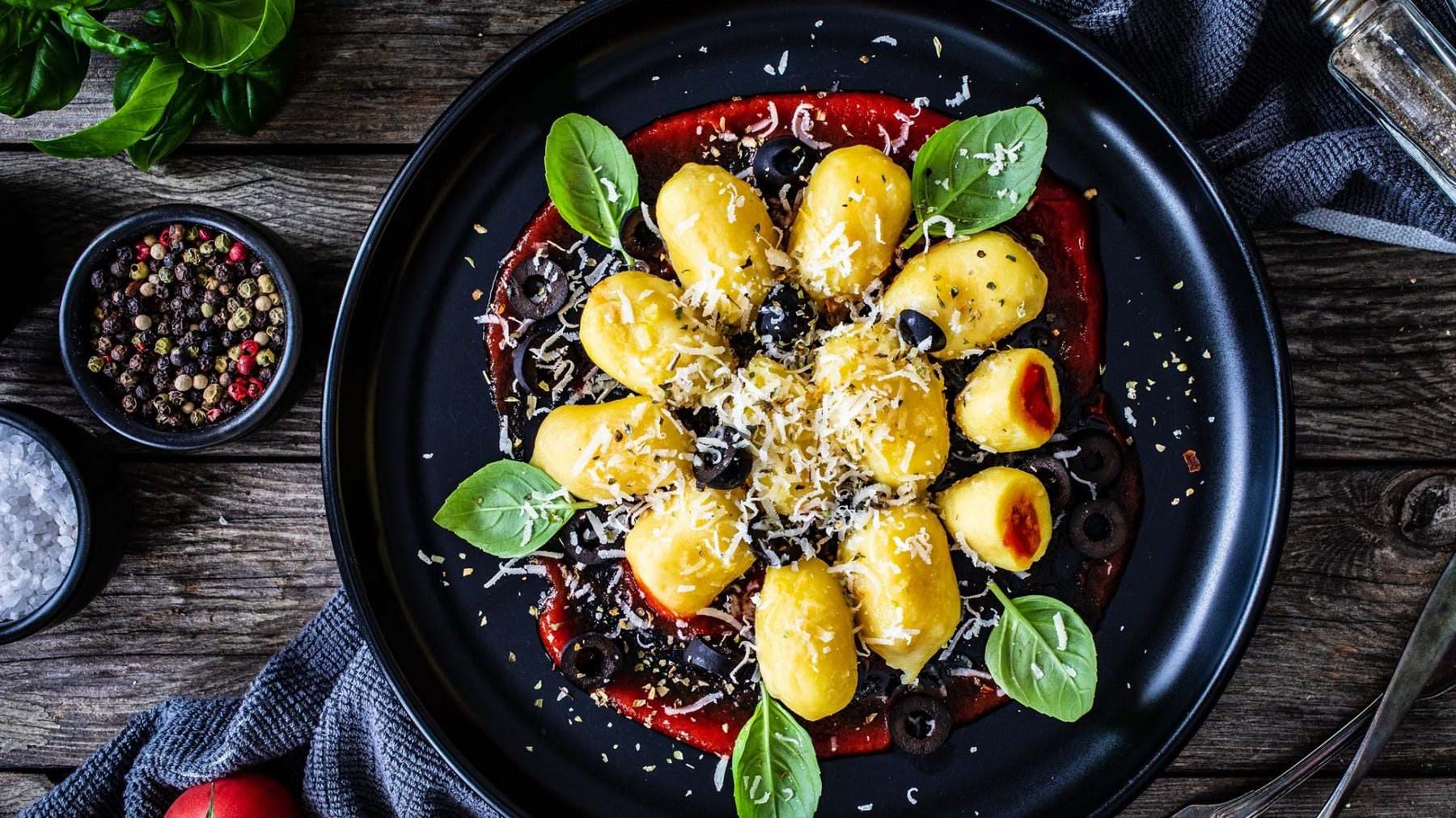 Ein Teller gefüllte Gnocchi mit rotem Pesto, Basilikumblättern, Parmesan und Oliven in der Draufsicht