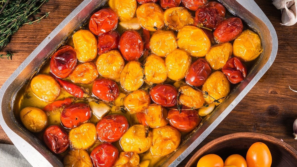 in einer ofenfesten form liegen geschmorte kirschtomaten mit thymian. drumherum liegen weitere tomaten. die tomaten sind gelb und rot.