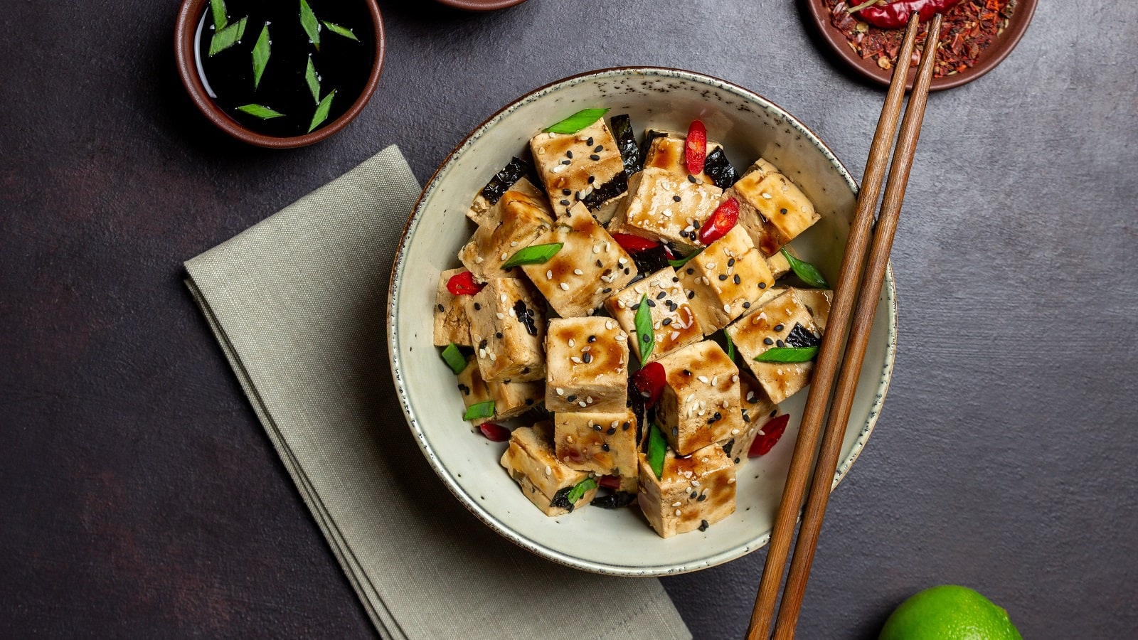 Ein runder Teller mit Tofu mit Teriyakisauce neben einem grauen Küchentuch
