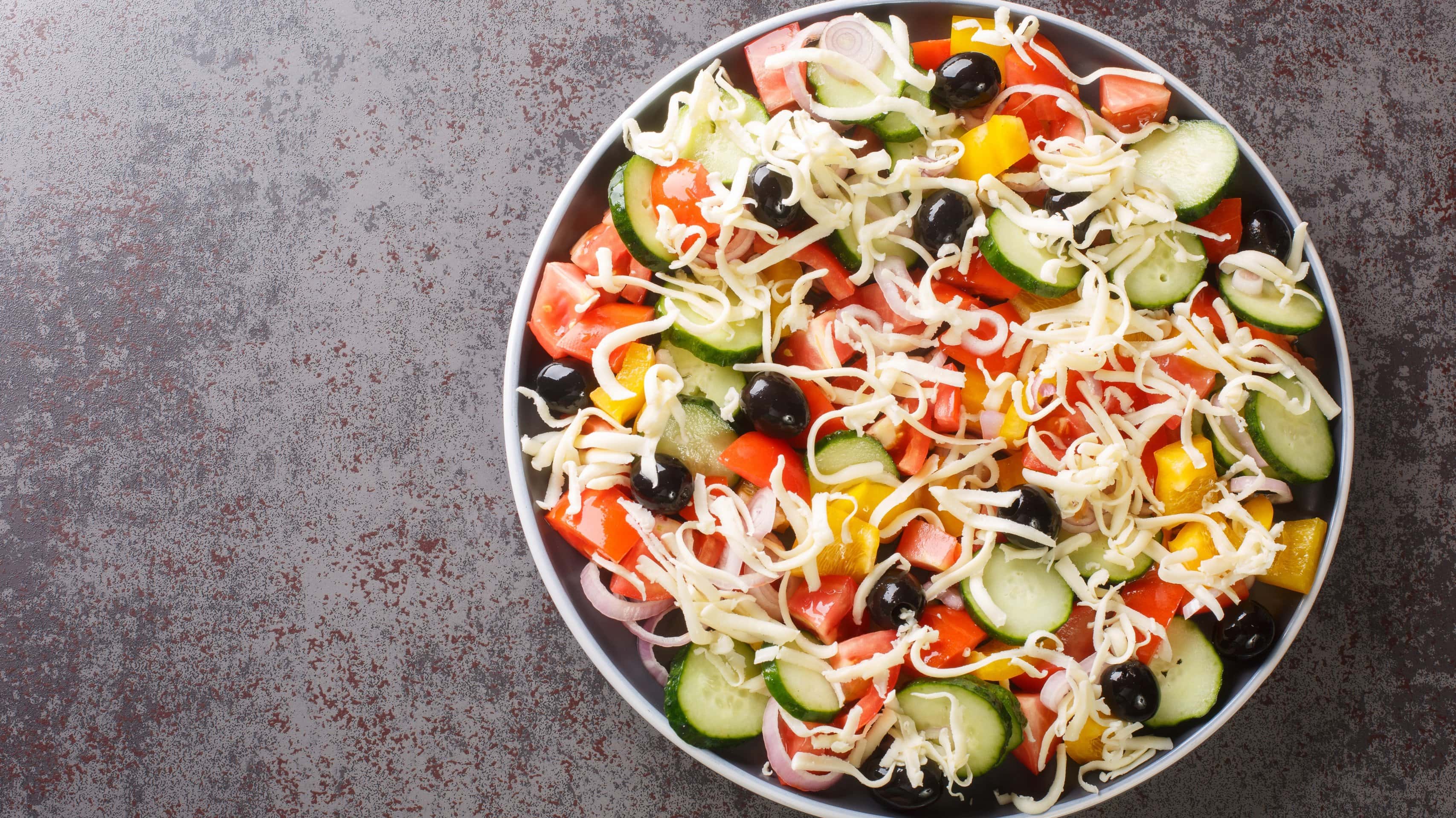 Eine großer Teller mit dem Shopska Salat auf einem grauen Untergrund aus der Vogelperspektive.