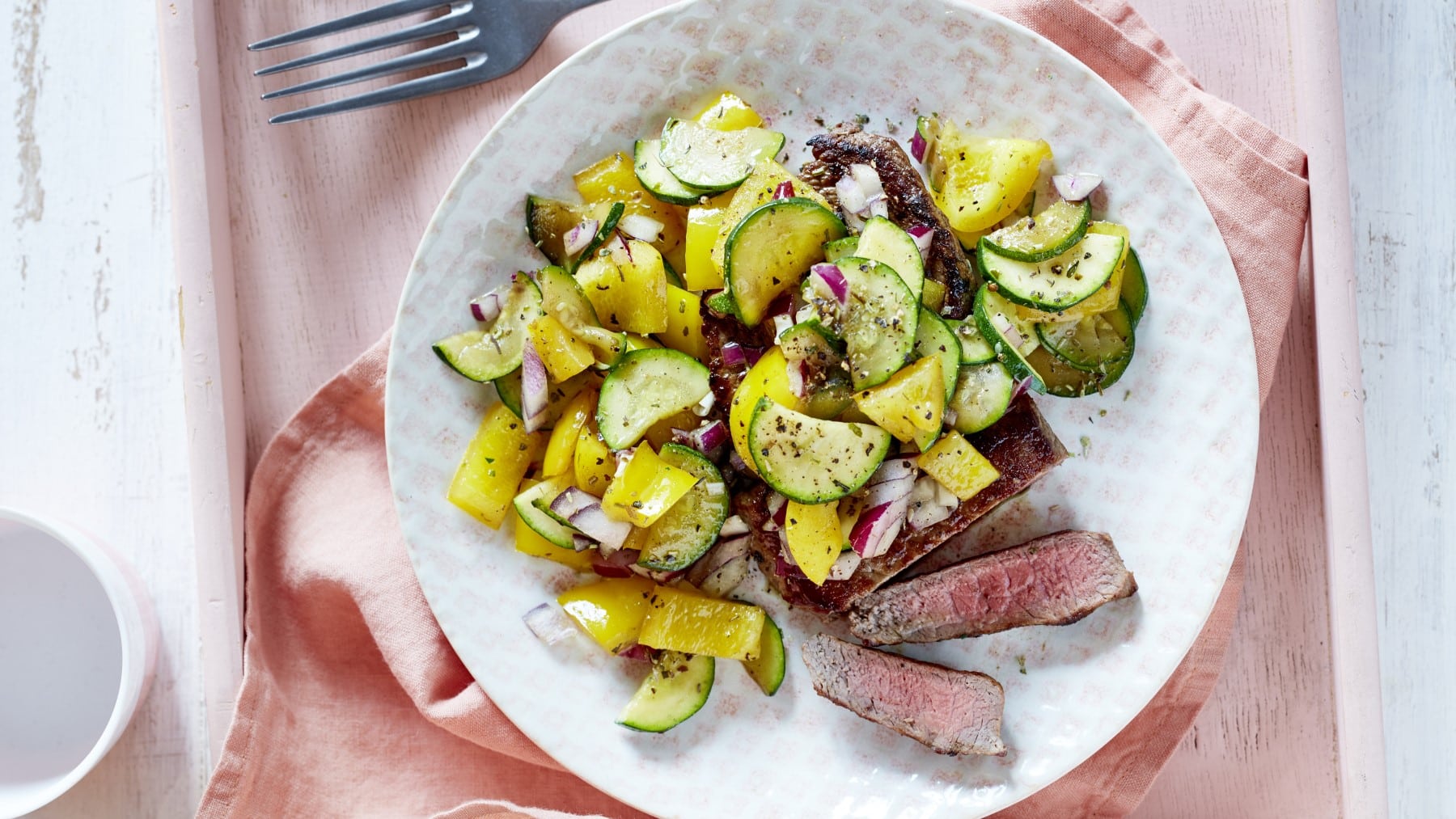 In Streifen geschnittenes Steak mit Mittelmeergemüse also Paprika und Zucchini auf einem runden Teller vor hellem Hintergrund