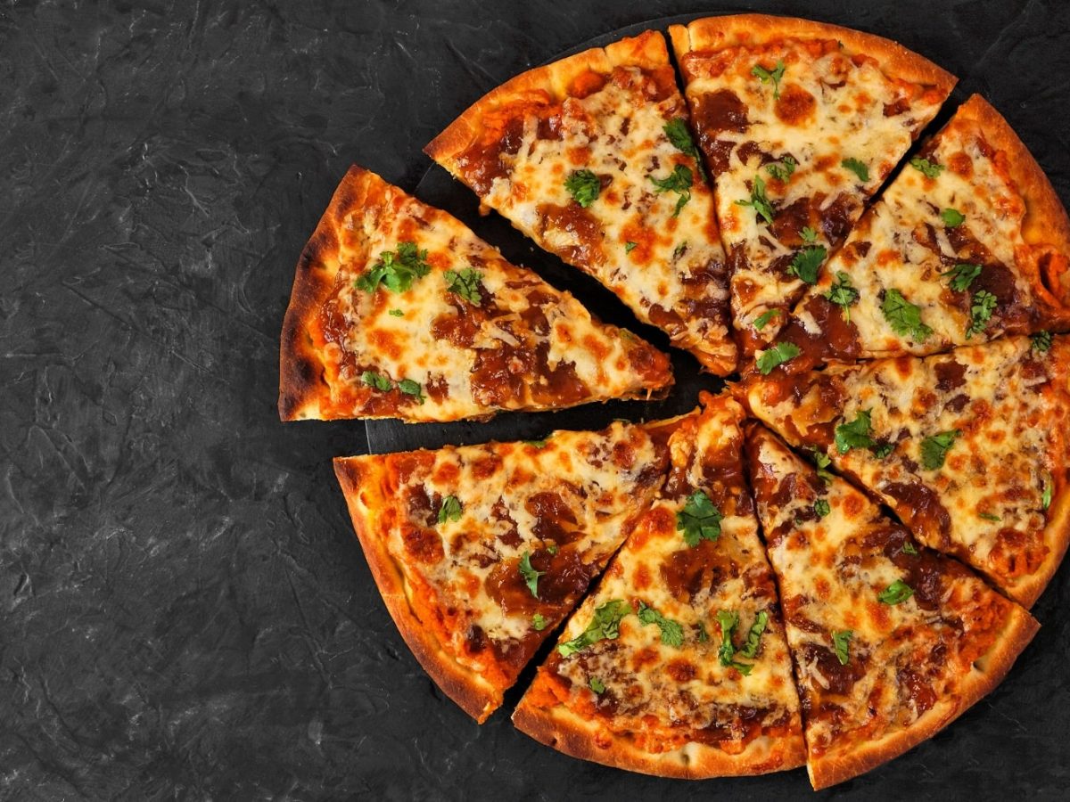 Eine geschnittene und reich belegte Pizza mit Süßkartoffel-Pizzateig auf dunklem Untergrund in der Draufsicht.
