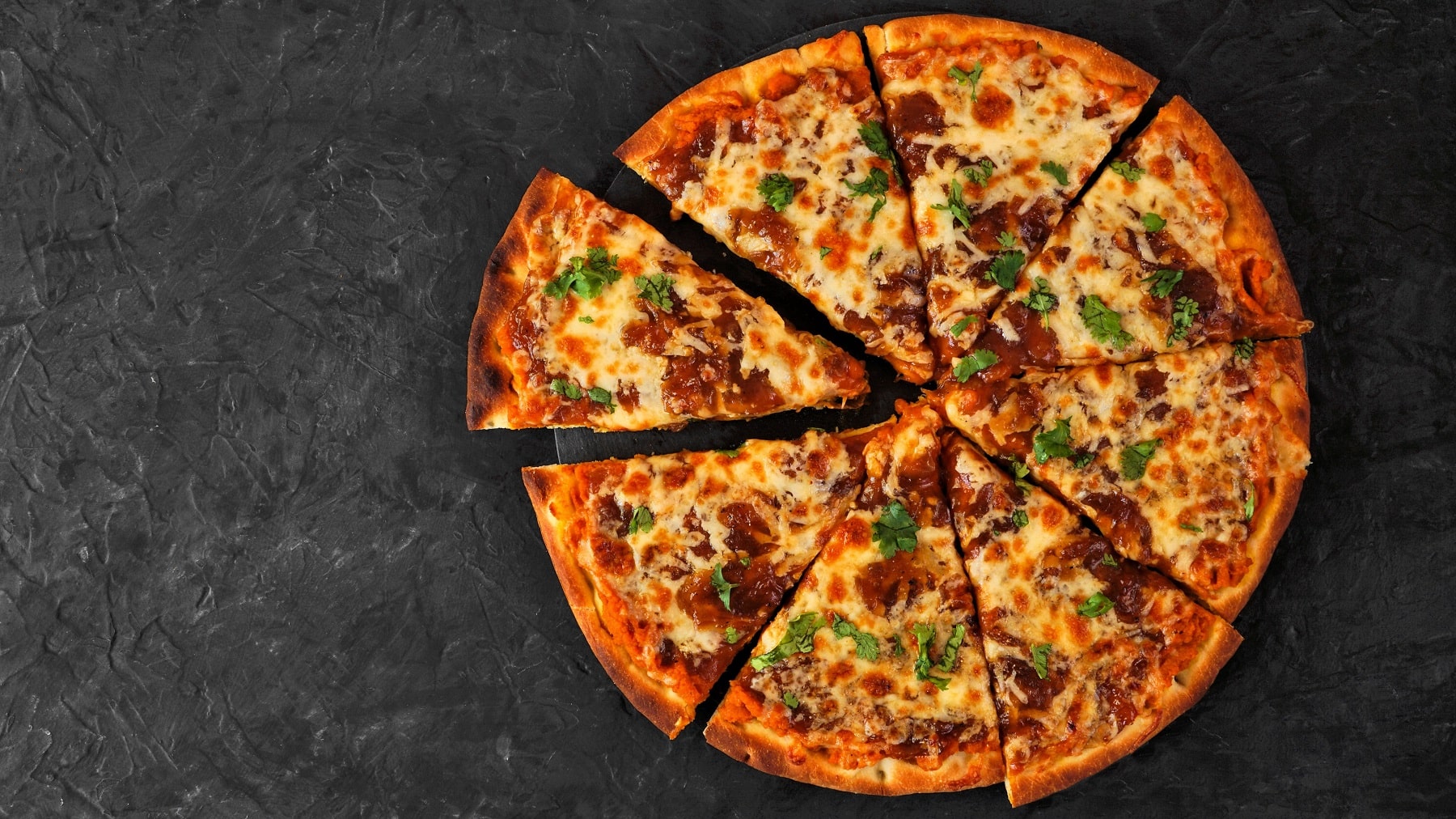 Eine geschnittene und reich belegte Pizza mit Süßkartoffel-Pizzateig auf dunklem Untergrund in der Draufsicht.