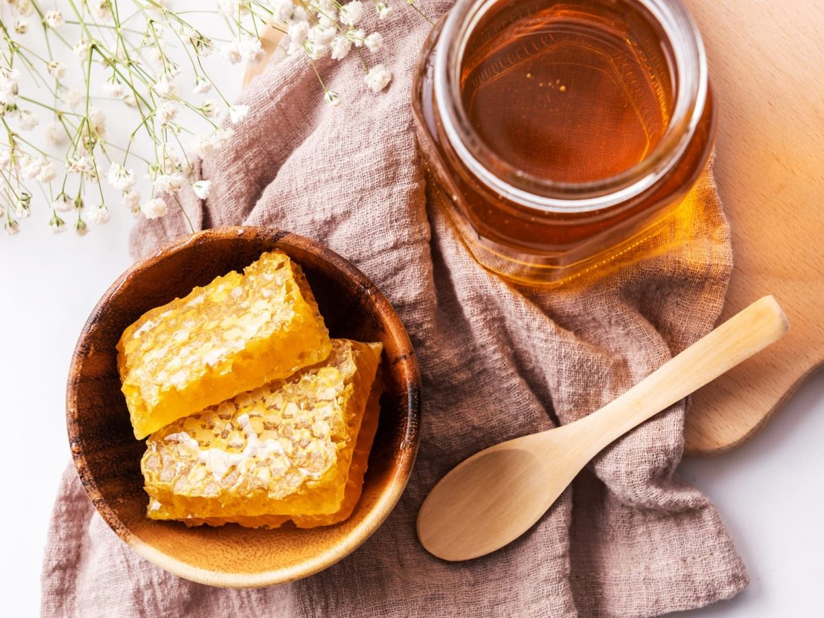Veganer Honig: Ein Glas mit Honig, daneben eine Schale mit Bienenwaben, in der Draufsicht.