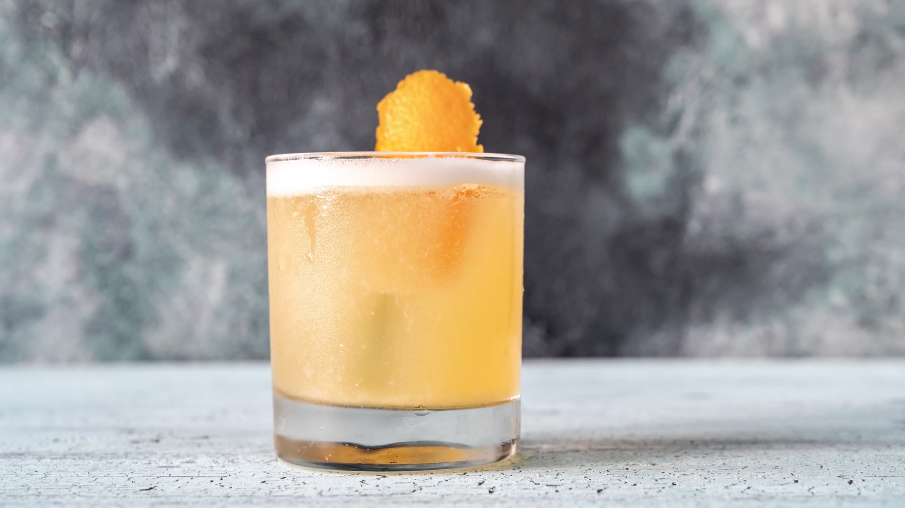 Ein Glas veganer Whiskey Sour mit einer Orangenzeste.