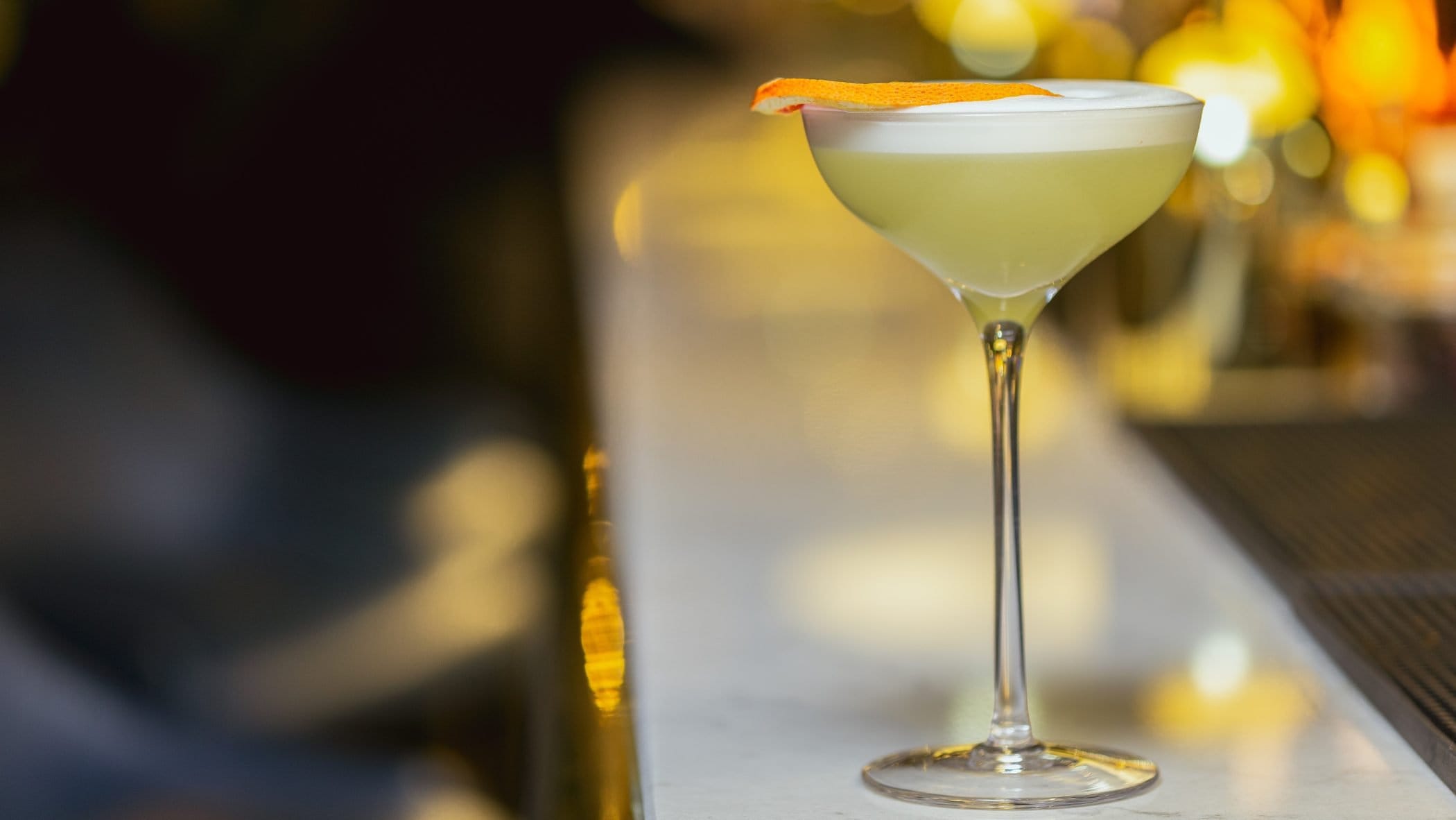 White Lady Cocktail auf Bartresen. Im Hintergrund unscharf eine Bar. Frontalansicht.