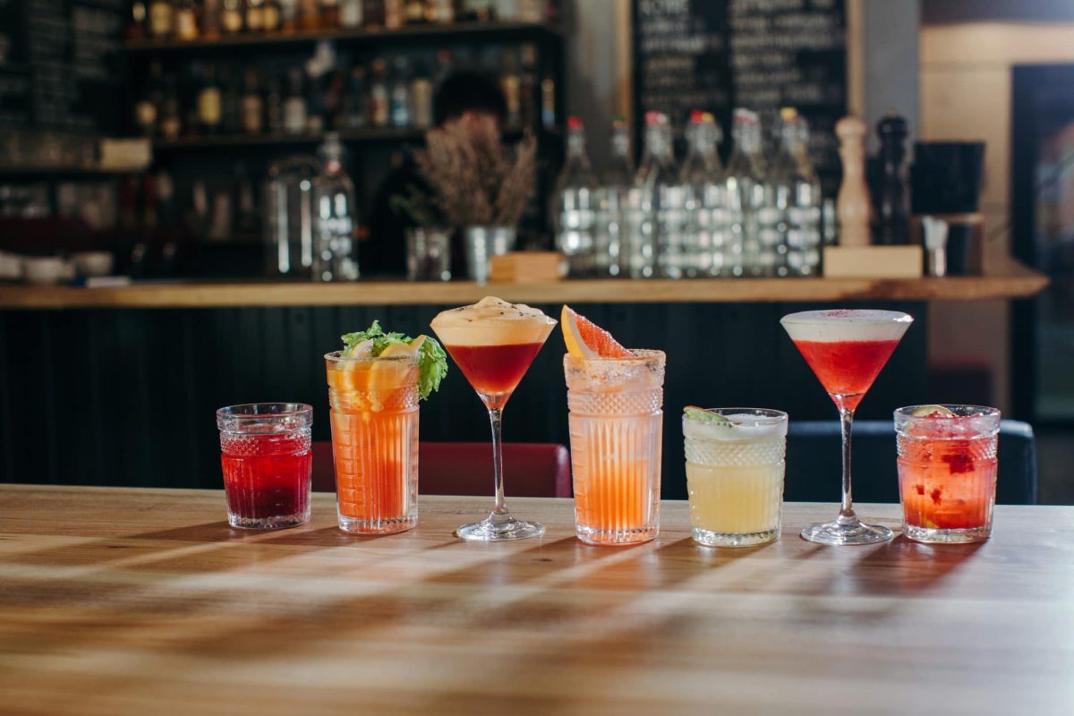 Cocktails verschiedene Sorten auf einem Tresen vor einer Bar. Frontalansicht.